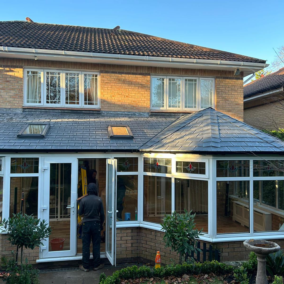 Person standing in a newly constructed conservatory of a house with a clear blue sky.